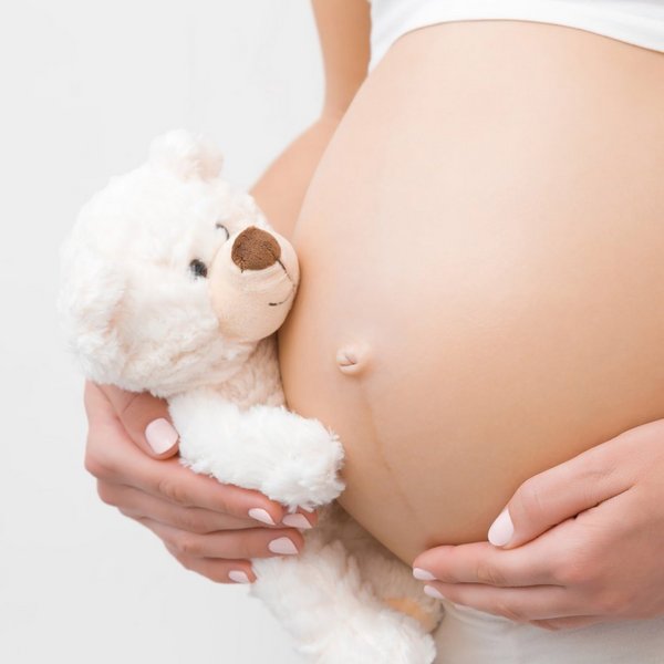 Mutter hält ihern schwangeren Bauch und einen weißen Kuschelbär